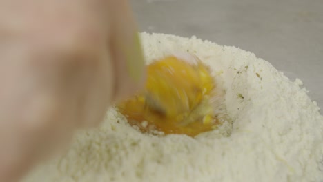 Mixing-egg-yolk-and-flour-using-fork-on-kitchen-cooking-table