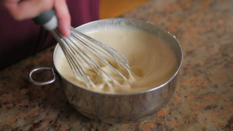 Close-up-of-a-hand-mixing-ingredients-in-a-steel-bowl-with-a-whisk