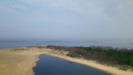 -Aerial-side-shot-of-Mikoszewskie-lake-and-Vistula-River-ended-in-sandbank-of-Mewia-Lacha-Nature-Reserve-during-a-sunny-day,-Baltic-Sea-in-background