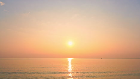 A-bright-yellow-sun-hangs-in-a-pink-and-yellow-sky-at-sunset-over-the-ocean-horizon