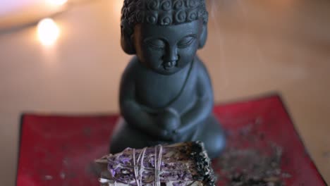 Kleine-Buddha-statue-Mit-Brennendem-Rauchendem-Lavendelsalbei,-Der-In-Zeitlupe-Auf-Roter-Asiatischer-Platte-Sitzt