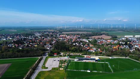AERIAL---Cityscape-of-Ebreichsdorf,-Austria-and-wind-turbines,-wide-shot-forward