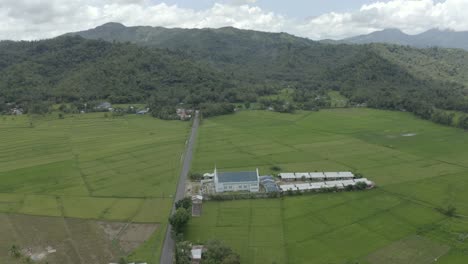 Vista-Idílica-De-Un-Pueblo-Junto-A-La-Carretera-Entre-Campos-Verdes-Y-Montañas-Forestales-Al-Fondo-En-El-Campo-De-Filipinas