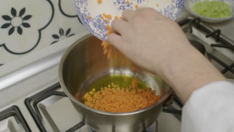Chef-adds-diced-carrots-into-metal-cooking-pot-with-olive-oil