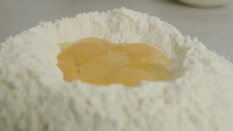Close-up-of-egg-yolks-inside-flour-ring-on-kitchen-cooking-table