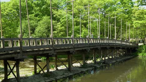 Alte-Holzbrücke-über-Den-Fluss-Mit-Grünen-Bäumen-Im-Hintergrund-Im-Koreanischen-Volksdorf-In-Yongin-City,-Seoul,-Südkorea
