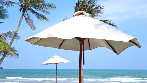 Weiße-Sonnenschirme-Bewegen-Sich-Unter-Dem-Wind-Am-Tropischen-Strand-In-Der-Lounge-Des-Hotelbereichs-Am-Meer