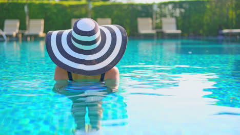 A-woman-in-a-swimming-pool-wearing-a-huge-floppy-straw-sun-hat-with-her-back-to-the-camera