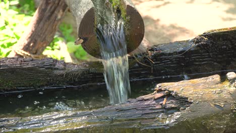 Water-flowing-through-open-wooden-pipes-filling-old-decrepit-wooden-water-mill-for-milling-wheat-and-rice-in-Korean-folk-village-Yongin-City,-Korea-close-up