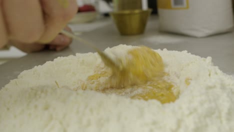 Mixing-egg-yolks-and-the-flour-using-fork-on-kitchen-cooking-table