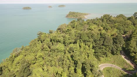 Aerial-fly-over-tropical-jungle-with-windy-road-,-ocean-and-tropical-islands-in-distance