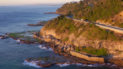 Sunset-View-At-The-Sea-Cliff-Bridge-Along-Pacific-Ocean-In-New-South-Wales,-Australia---aerila-drone-shot