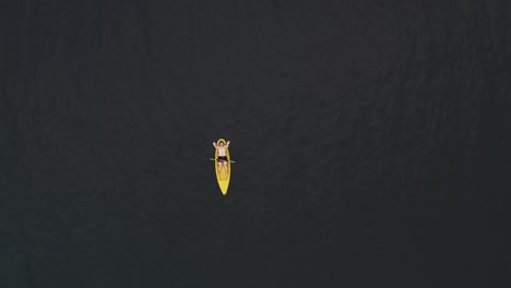 Mann,-Der-Auf-Einem-Gelben-Kanu-Liegt,-Das-Im-Meer-Schwimmt-Und-Mit-Den-Händen-Auf-Der-Drohne-Winkt