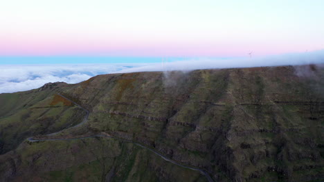 Drone-aerial-footage-of-clouds-swopping-across-mountains-in-Madeira,-Portugal-with-wind-turbines
