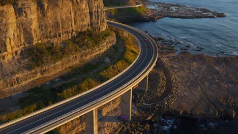 Flying-Towards-Sea-Cliff-Bridge-With-Cars-Driving-On-Rocky-Coastline-In-Northern-Illawarra-Region-Of-New-South-Wales,-Australia