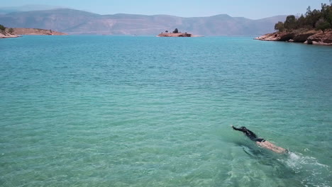 A-young-woman-swims-effortlessly-through-the-brilliant-aquamarine-waters-of-the-Gulf-of-Corinth,-Greece