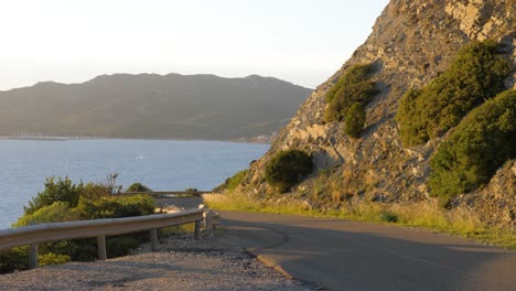Slow-motion-shot-of-afternoon-sun-on-curvy-asphalt-road-on-the-coastline-with-cliffs-in-Chia,-Southern-Sardinia,-Italy