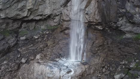 Man-is-standing-near-waterfall-Almenbachfall-Berner-Oberland-Switzerland-drone-flight