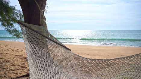 Close-up-of-an-empty-woven-hammock-on-a-deserted-beach-overlooking-the-ocean-waves