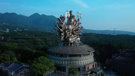 Aerial-flight-towards-Guanyin-goddess-Silver-Temple-Statue-against-mountain-landscape-and-blue-sky-in-backdrop