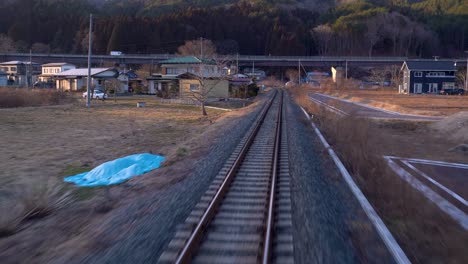 View-from-back-of-train-riding-through-Japanese-countryside-with-few-houses