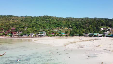 Colorful-village-in-Phi-Phi-Don-island-with-people-on-beach-shoreline-and-forest-at-background