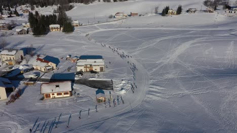 Aerial-flyover-Lajoux-village-with-snow-covered-houses-beside-biathlon-skiing-race-during-sunlight-in-winter