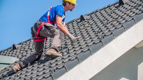 Male-roofer-with-safety-bell-removes-roof-tiles-for-solar-panel-construction