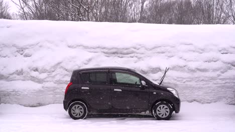 Kleines-Auto,-Das-In-Winterlicher-Landschaft-Gegen-Eine-Hoch-Aufragende-Schneewand-Geparkt-Ist