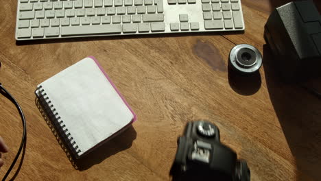 Hand-takes-DSLR-camera-and-notepad-from-computer-desk-in-morning-light