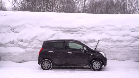 Black-car-parked-against-very-high-snow-wall-with-snow-falling-in-slow-motion