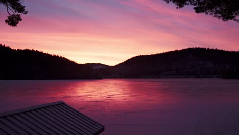 Colorful-Pink-Sunset-Reflecting-On-Frozen-Lake-With-Silhouette-Mountain-In-Norway