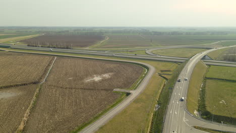 Aerial-shot-of-agricultural-growing-fields-beside-highway-with-much-traffic,-exhaust-gases-and-environmental-pollution
