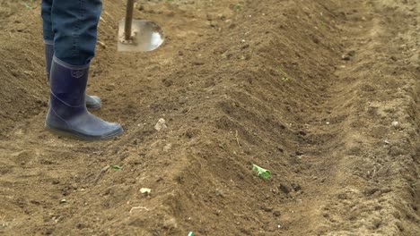 Man-in-rubber-boots-dig-the-soil-in-the-garden-making-grooves,-Farmer-cultivating-brown-soil-using-Garden-hoe-in-South-Korea-close-up