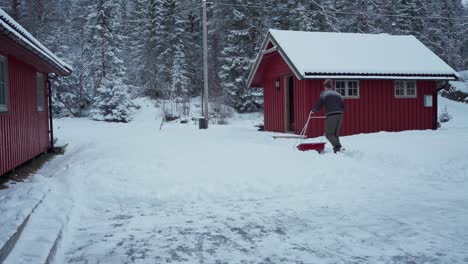Hombre-Limpiando-El-Patio-Trasero-En-Nieve-Profunda-Usando-Una-Pala-De-Trineo-Cerca-Del-Campo-De-Trondheim-En-Noruega