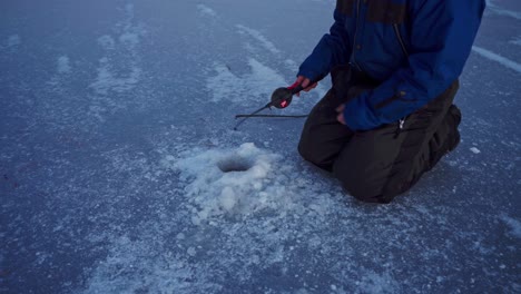 Hombre-Con-Caña-De-Pescar-Atrapa-Peces-En-Un-Agujero-De-Hielo-En-Un-Lago-Congelado-En-Trondheim,-Noruega