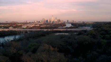 Downtown-Austin,-Texas-skyline-revealed-from-behind-trees-at-Sunset,-drone-aerial-4k