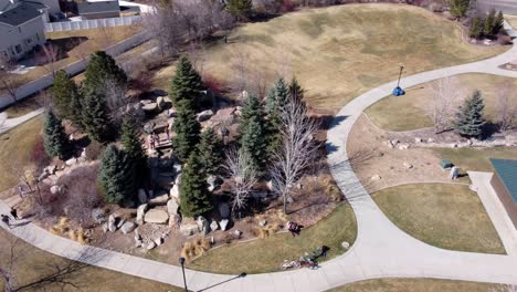 Drone-flying-in-circles-around-a-public-rock-park-with-playground,-revealing-suburban-middle-class-American-neighborhood,-while-children-play,-on-a-sunny-spring-day-after-covid-19-lockdown-lifts