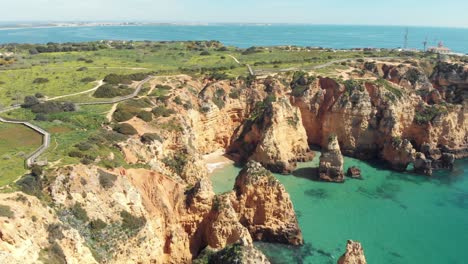 Emerald-Green-sea-bathing-Ponta-da-Piedade-cliffs-in-Lagos-Algarve,-Portugal---Wide-establishing-slide-tilt-up-shot
