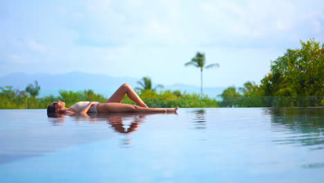 Woman-sunbathing-lying-in-water-on-edge-of-infinity-pool