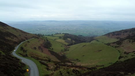 White-vehicle-driving-narrow-single-rural-road-running-through-Welsh-green-mountain-valleys-landscape