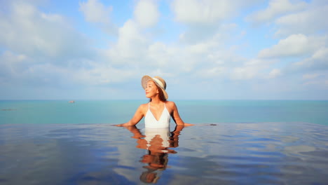 Young-Asian-woman-with-hat-relaxing-in-infinity-pool-with-horizon-in-background