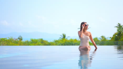 Charming-Asian-woman-sitting-in-infinity-pool-water-with-elegant-swimsuit