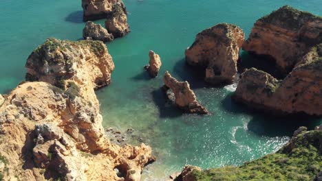 Pointy-golden-rock-formations-sprouting-from-Algarve-blue-sea-in-Lagos,-Portugal---Aerial-top-rotation-view