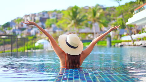 Back-view-of-woman-in-pool-with-white-hat-raising-arms