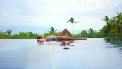 Lying-on-the-shallow-edge-of-a-resort-swimming-pool-a-young-woman-with-a-bent-leg-enjoys-the-tropical-sun