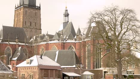 Slow-pan-showing-the-remains-of-the-medieval-city-wall-revealing-the-Drogenapstoren-rising-above-winter-barren-trees-part-of-the-cityscape-of-Hanseatic-city-Zutphen,-The-Netherlands,-covered-in-snow