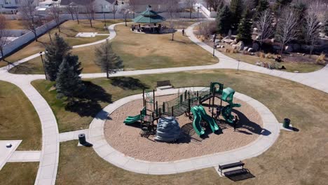 Drone-shot-flying-in-counter-clockwise-circle-over-a-public-park-with-children’s-playground,-revealing-houses-and-upper-middle-income-American-neighborhood