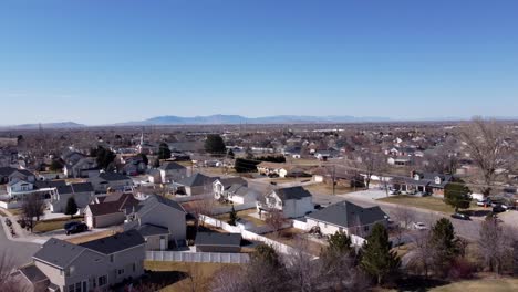 Drone-flying-straight-up-focusing-on-a-leafless-tree-from-winter-to-reveal-a-beautiful-American-suburban-neighborhood-with-mountains-in-the-distant-background-on-a-sunny-spring-day