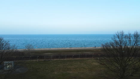 Aerial-View-Calm-Blue-Sea-From-A-Park-With-A-Person-Walking-At-Promenade-In-The-Morning-Near-Westerplatte,-Gdansk,-Poland